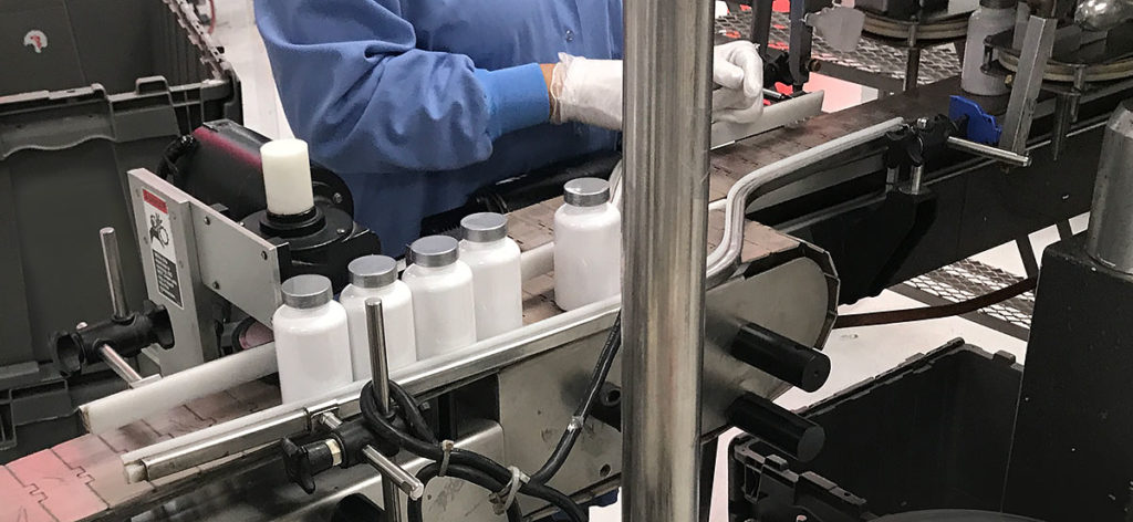 Worker handling supplement bottles on a conveyor belt in Vitaquest's packaging facility.