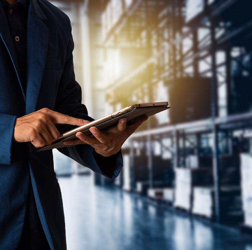 Man in a dark suit using a tablet in a sunlit warehouse.