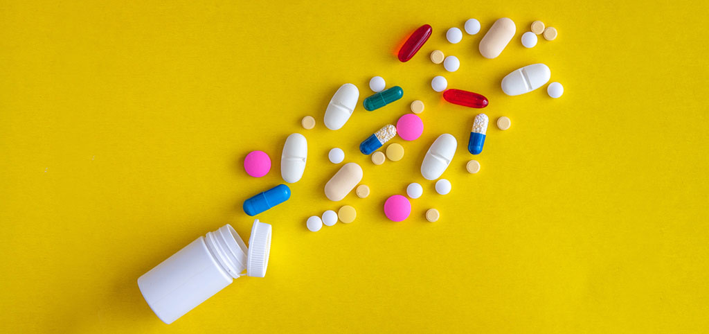 Capsules and pills spilled from a white bottle on a yellow background,