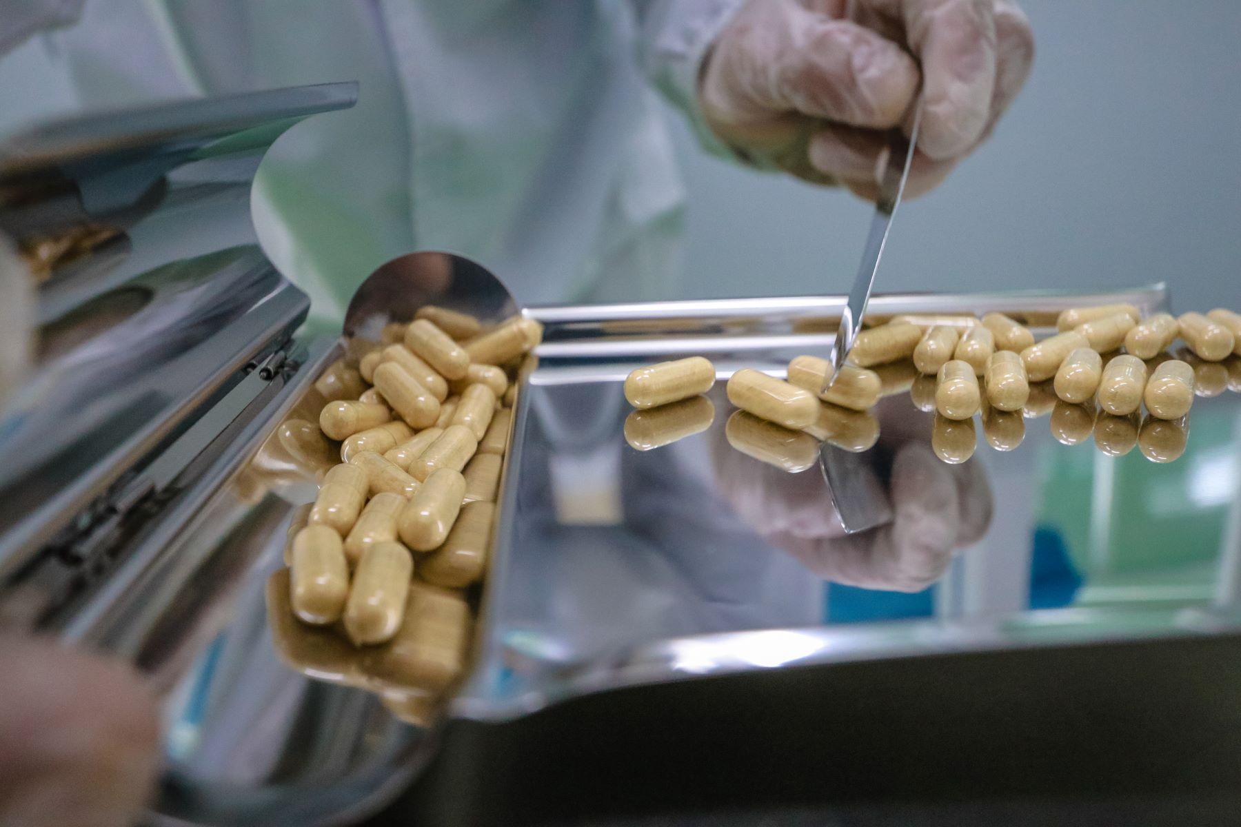 Close-up of gloved hands sorting yellow capsules with precision tools on a capsule manufacturing line.