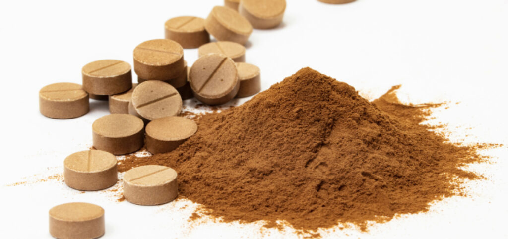 Brown supplement tablets with corresponding powder heap on white background.