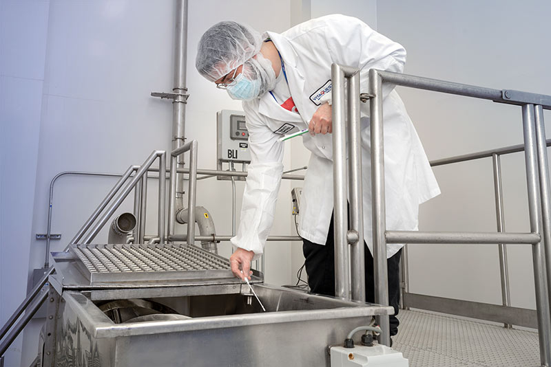 Lab technician in protective gear inspecting machinery in a sterile environment.