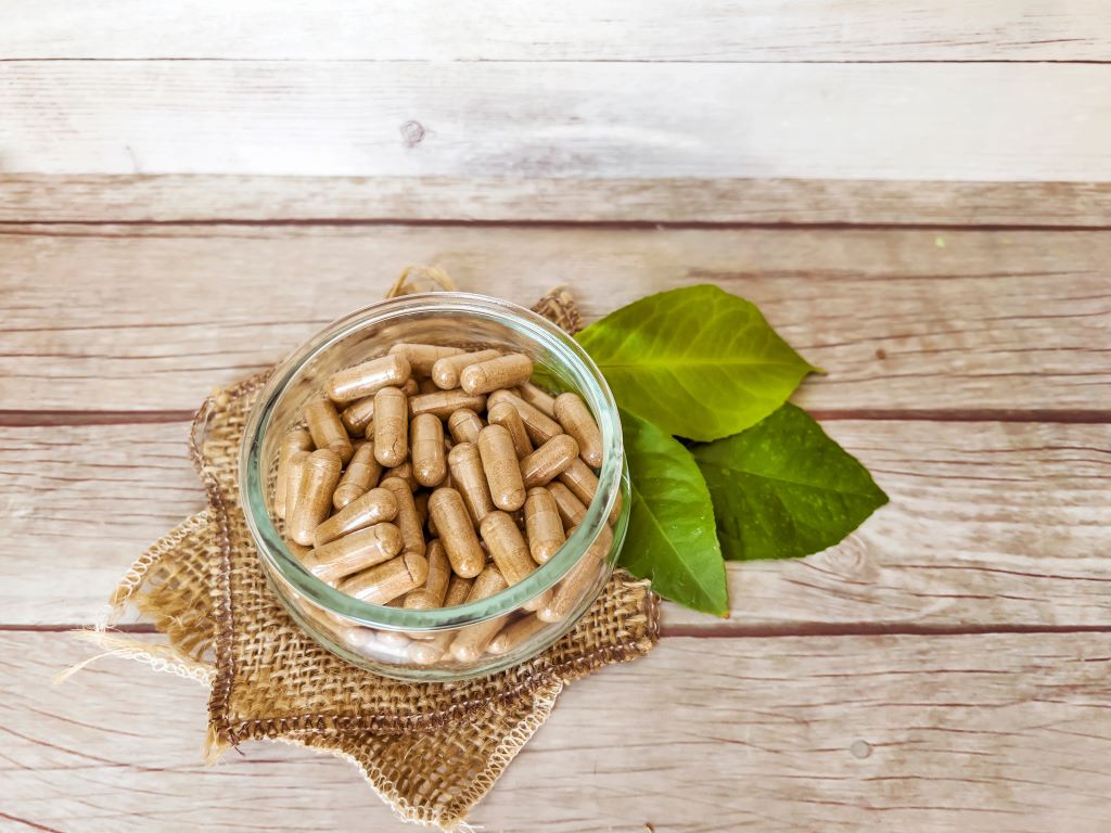 A collection of ashwagandha capsules in a bowl that's placed on a wooden table.