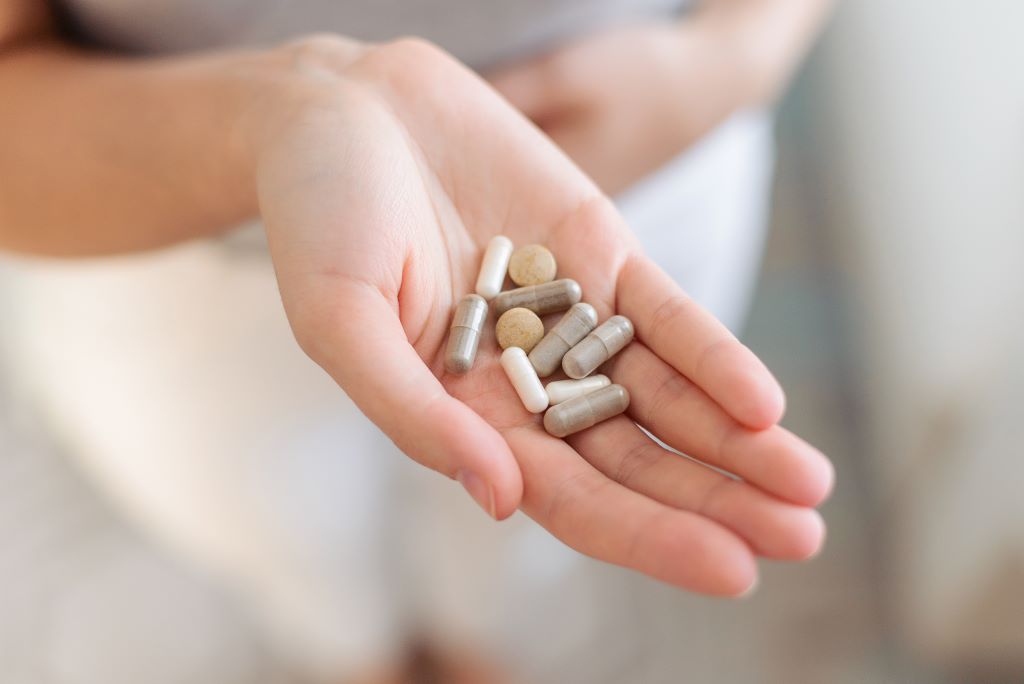 Assorted capsules and tablets in a person's hand.